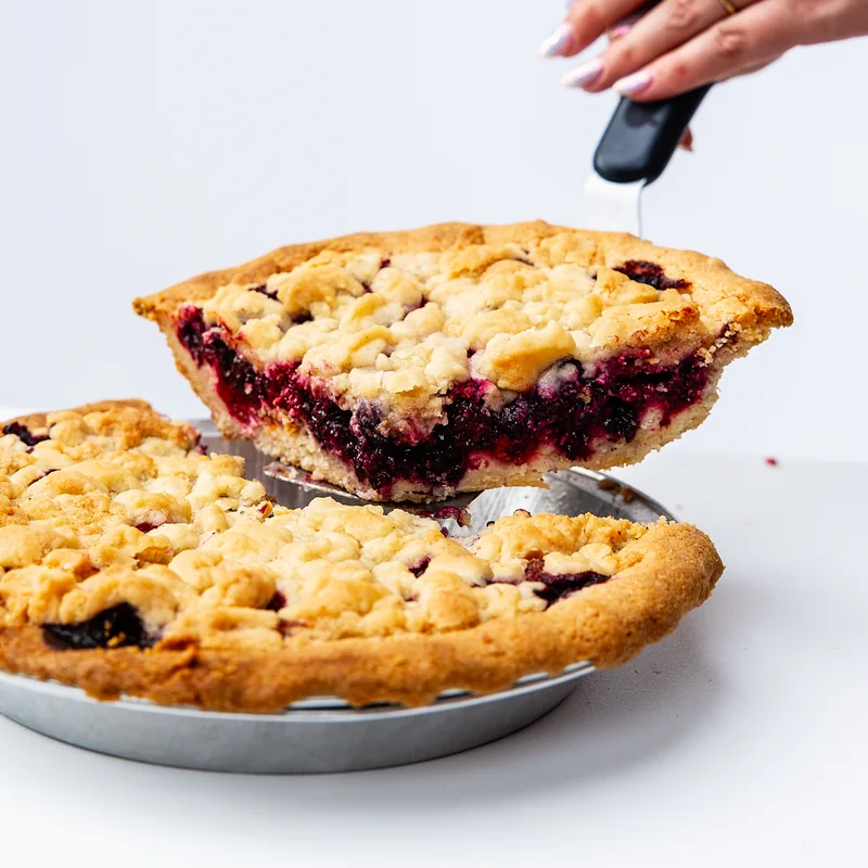 A deep berry-filled slice lifted above a golden crumble pie